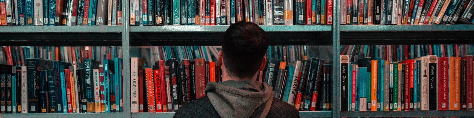 person wearing black and gray jacket in front of bookshelf